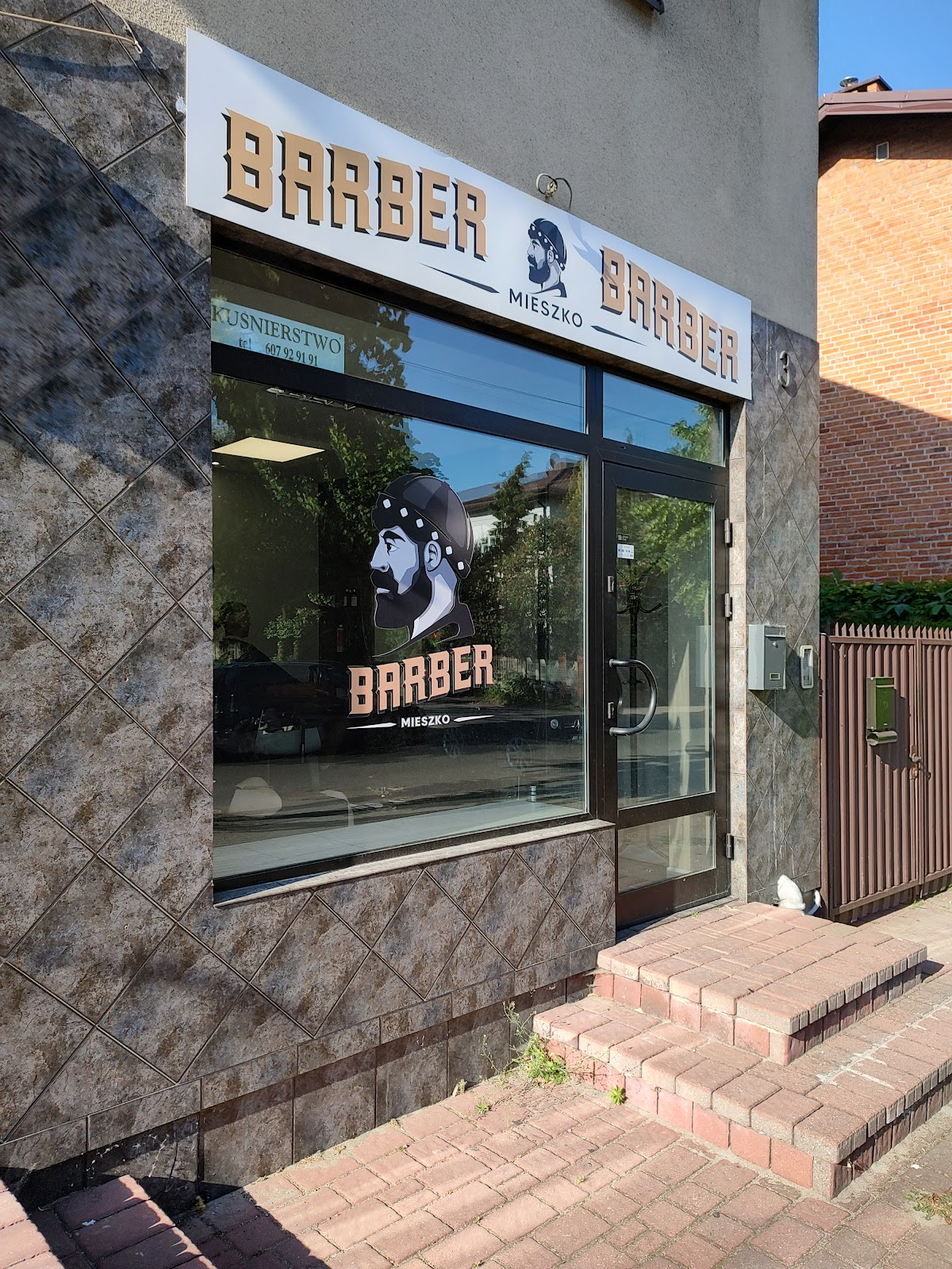 Wejście do Barber Mieszko w Łasku z szyldem i logo w witrynie